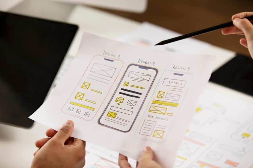 Hand holding paper with three mobile wireframe designs